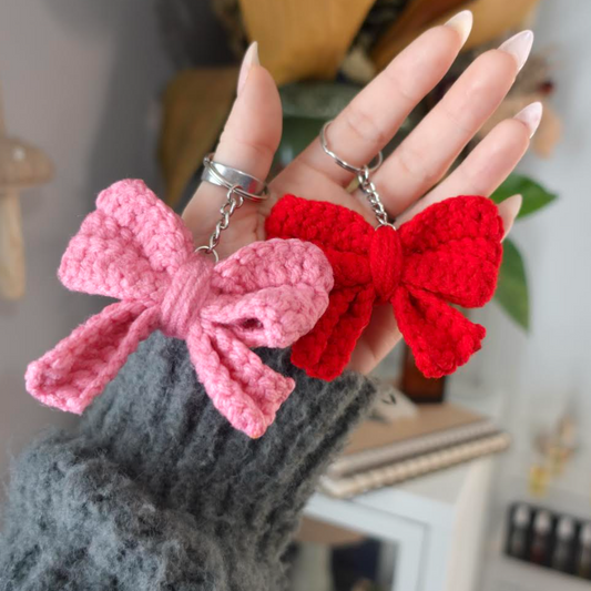 Two bow keychains held in hand left side pink right side red crochet